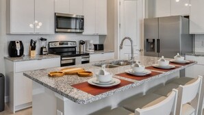 Una cocina moderna con gabinetes blancos, microondas de acero inoxidable, cafetera y una isla grande con taburetes de bar.