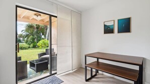 A room with a sliding glass door leading to a patio, a wooden bench, and two framed pictures on the wall. - Charming Townhouse Near Indialantic Beach (Indialantic)