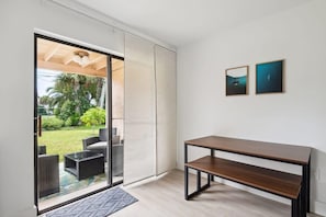 A modern room with a sliding glass door leading to a patio area with outdoor furniture. There is a wooden bench against the wall and two framed pictures on the wall. - Charming Townhouse Near Indialantic Beach (Indialantic)
