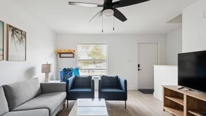 A modern living room with a ceiling fan, a sofa, a coffee table, and a television on a wooden stand. - Charming Townhouse Near Indialantic Beach (Indialantic)