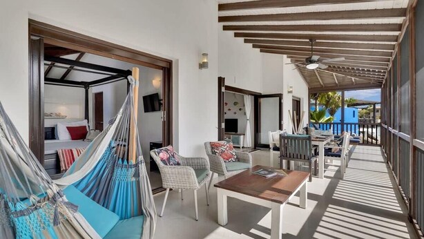 A covered outdoor area with a hammock, wicker chairs, a wooden table, and a ceiling fan. - Casa de las Brisas with Large Communal Pool (Kralendijk)