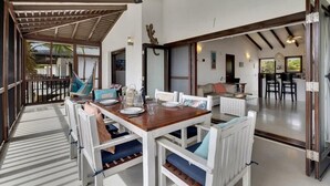A dining area with a wooden table and white chairs, a ceiling fan, and a view of the outdoor space. - Casa de las Brisas with Large Communal Pool (Kralendijk)