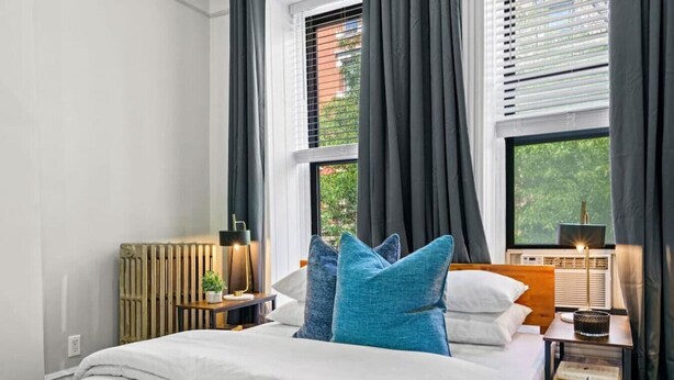 A bedroom with a bed, a nightstand, a lamp, and a window with curtains. - Spacious 3-Bed Brownstone, near Columbia Uni (New York)