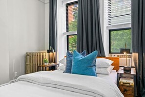 A bedroom with a bed, a nightstand, a lamp, and a window with curtains. - Spacious 3-Bed Brownstone, near Columbia Uni (New York)