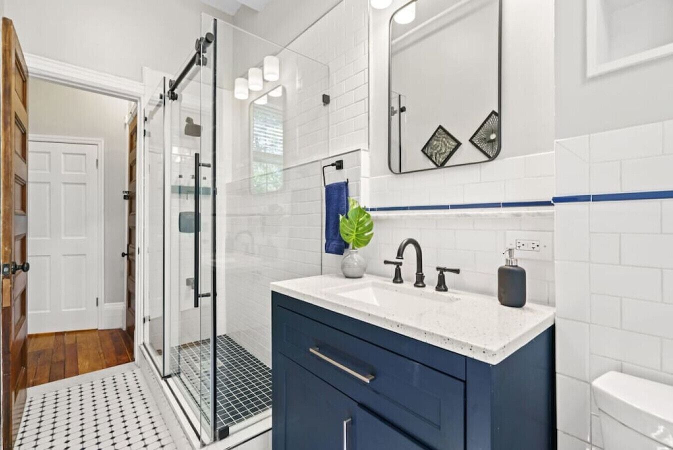 A modern bathroom with a glass shower enclosure, a white sink with a blue countertop, and a dark blue vanity.