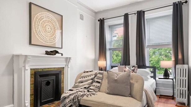 Un dormitorio con chimenea, un sofá, una cama y ventanas grandes con cortinas.