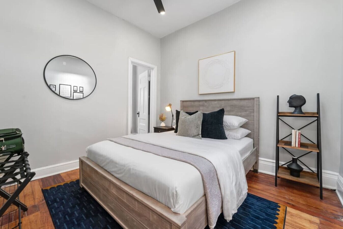 A modern bedroom with a large bed, a round mirror, a bookshelf, and a door.