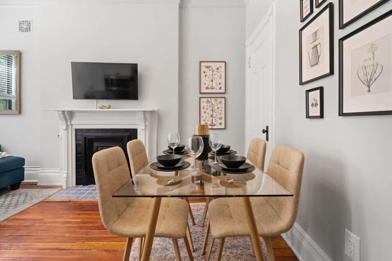 Comedor con mesa de vidrio, cuatro sillas, chimenea y cuadros en la pared.