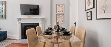 Comedor con mesa de vidrio, cuatro sillas, chimenea y cuadros en la pared.