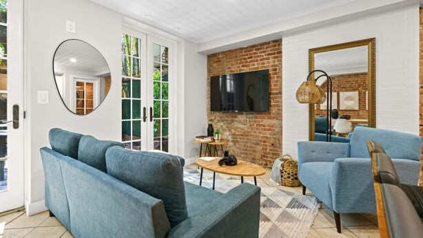 A modern living room with two blue sofas, a TV mounted on a brick wall, and a large mirror.