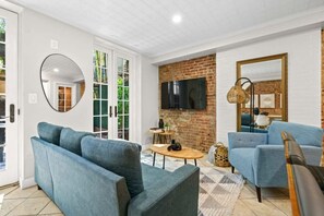 A modern living room with two blue sofas, a TV mounted on a brick wall, and a large mirror. - Family Brownstone with Private Backyard Near Subway (New York)