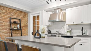 A modern kitchen with white cabinets, a large island, and a brick wall.