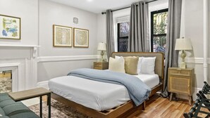 A bedroom with a wooden bed, two bedside tables, a nightstand, a fireplace, and a window with curtains.