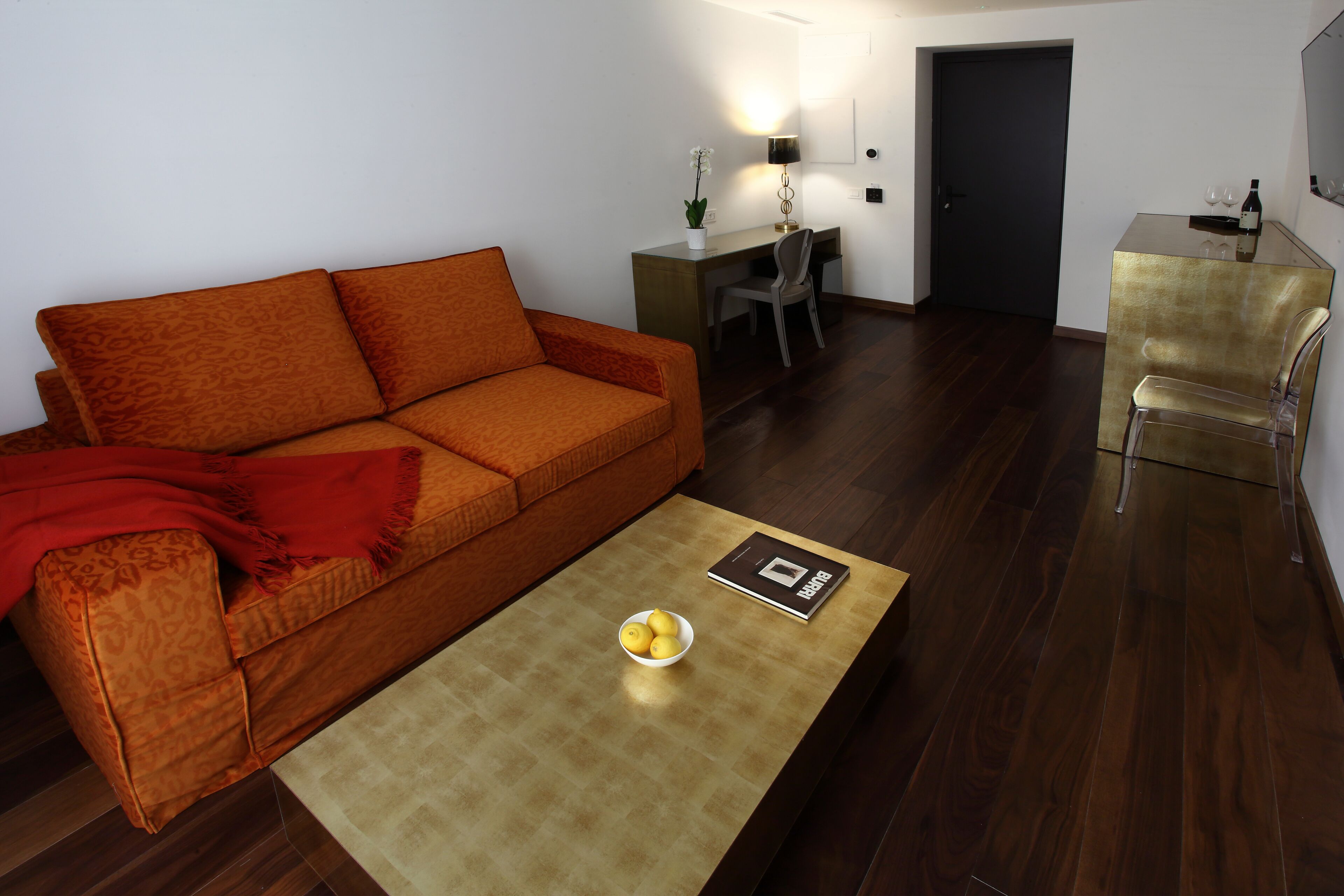 A modern living room with a sofa, a coffee table with a bowl of lemons, a desk with a chair, and a dining area with a chair.