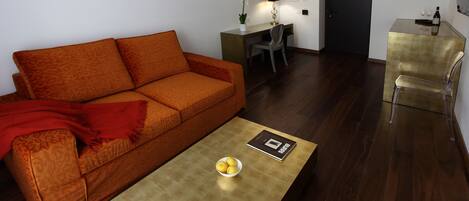 A modern living room with a sofa, a coffee table with a bowl of lemons, a desk with a chair, and a dining area with a chair.