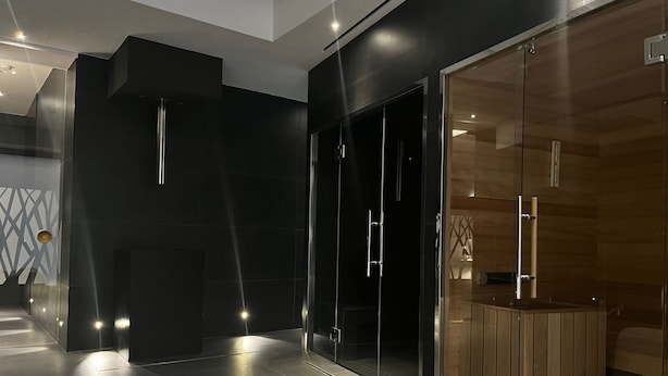 A modern hotel room with a large sliding glass door leading to a wooden sauna area, a black accent wall, and a white sofa. - PALAZZO CARTARI (Palermo)