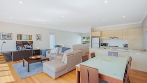 A modern living room with a sofa, coffee table, and dining table. There is a kitchen area with cabinets and appliances.