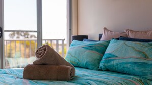 Un lit avec une serviette roulée, une literie aux motifs turquoise et bleu, et une vue sur un balcon avec une balustrade.
