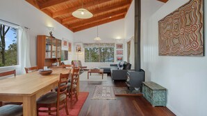 A modern living room with a wooden dining table, chairs, a sofa, and a fireplace. - 129 Murrah Street - River Views (Bermagui)