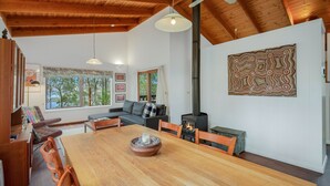 A cozy living room with a wooden dining table, a sofa, and a fireplace. - 129 Murrah Street - River Views (Bermagui)