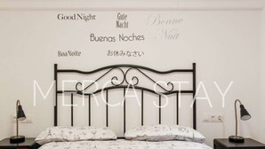 A bedroom with a bed, two bedside tables, and a wall with multilingual "Good Night" signs. - Cozy Apartment in Sitges (Sitges)