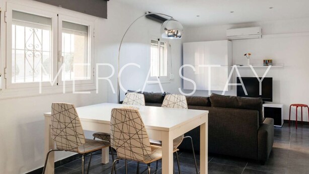 A modern living room with a dining area, featuring a sofa, a TV, and a dining table with chairs. - Cozy Apartment in Sitges (Sitges)