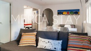 A modern living room with a grey sofa, striped pillows, and a ceiling light fixture. - Cozy Apartment in Sitges (Sitges)