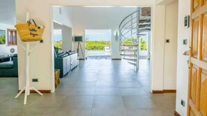 A spacious interior with a staircase leading to a balcony, a seating area with a view, and a wall-mounted basket. - Whispers of the Caribbean: Villa Azur’s Private Pool, Jacuzzi & Timeless Luxury (Collectivité de Saint-Martin)