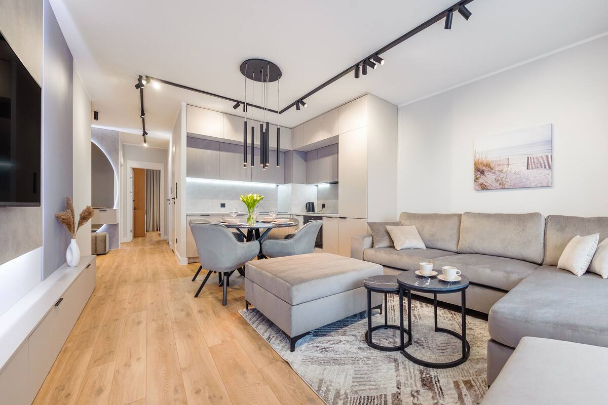 A modern living room with a grey sofa, a coffee table, and a dining area with a table and chairs.