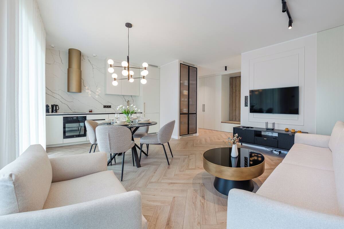 A modern living room with a dining area, a kitchen, and a TV mounted on the wall.