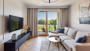 A modern living room with a large flat-screen TV, a sofa, a coffee table, and a balcony with a view of greenery. - Apartamenty Sun & Snow Porto (Gdansk)