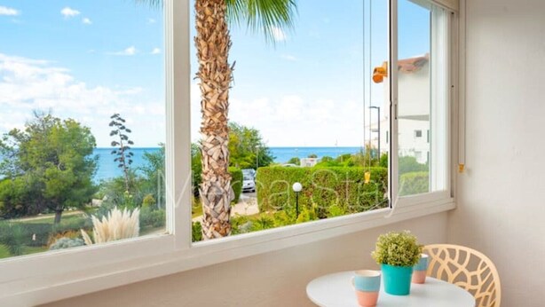 Ein Balkon mit Meerblick, eine Palme, ein Tisch mit Stühlen und einer kleinen Pflanze.