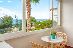 Un balcón con vista al mar, una palmera, y una mesa con sillas y una planta pequeña.