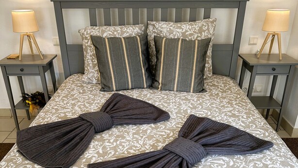Ein Bett mit grauem Kopfteil, zwei Nachttischen und einer gemusterten Bettdecke.