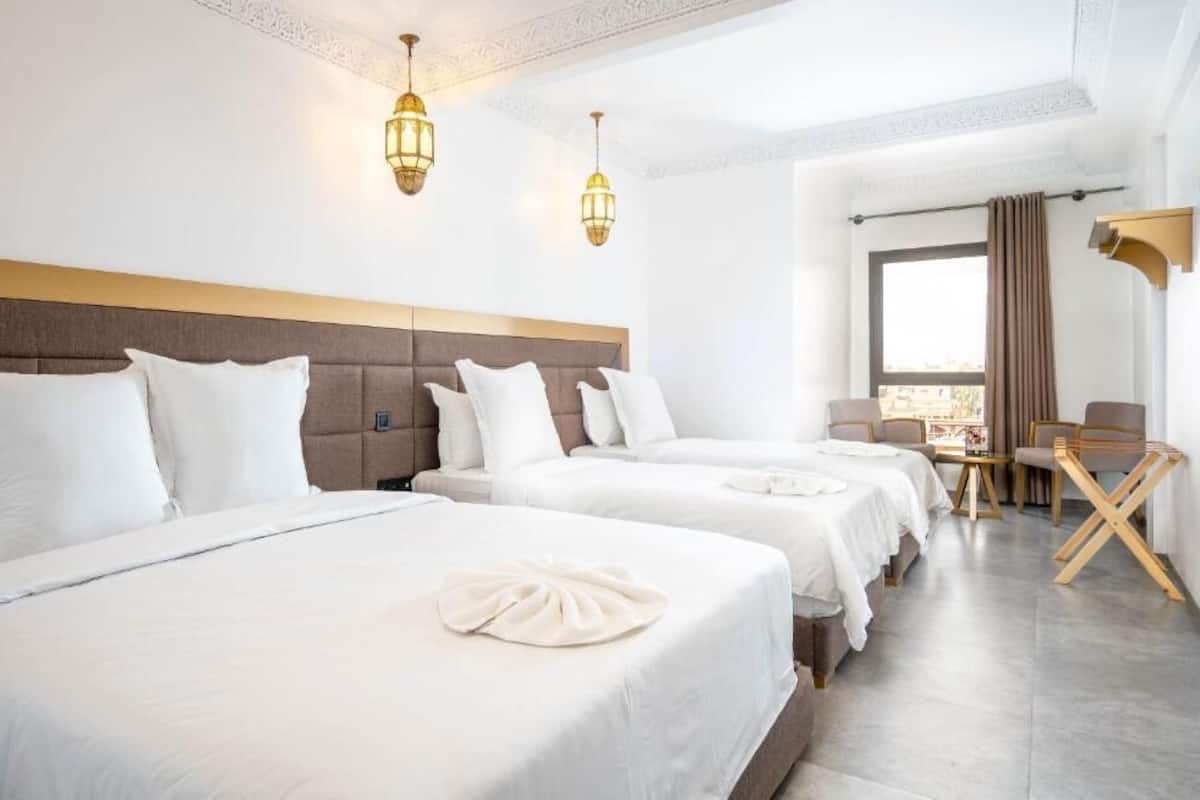 Hotellihuone, jossa on kolme sänkyä, ruokailutila ja näkymä kaupunkiin.