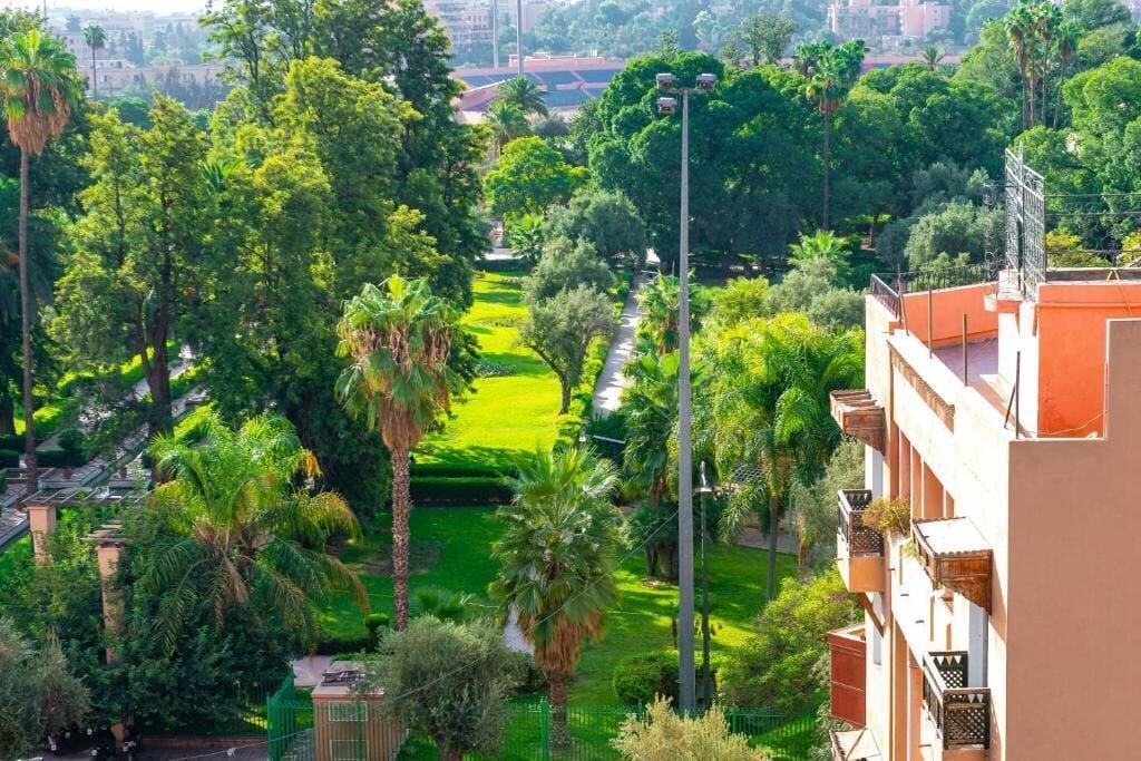 Un parc verdoyant et luxuriant, doté d’un sentier, entouré de grands arbres et bordé d’un immeuble avec des balcons.