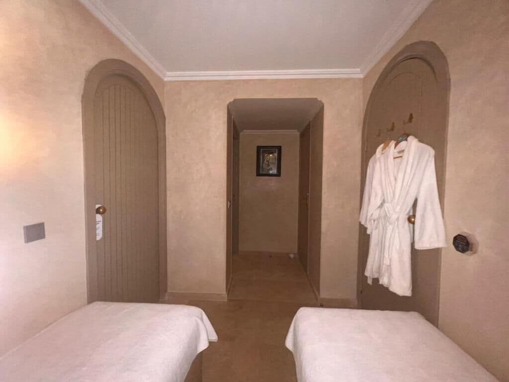 A hotel room with two single beds, a door with a handle, and a robe hanging on the wall.