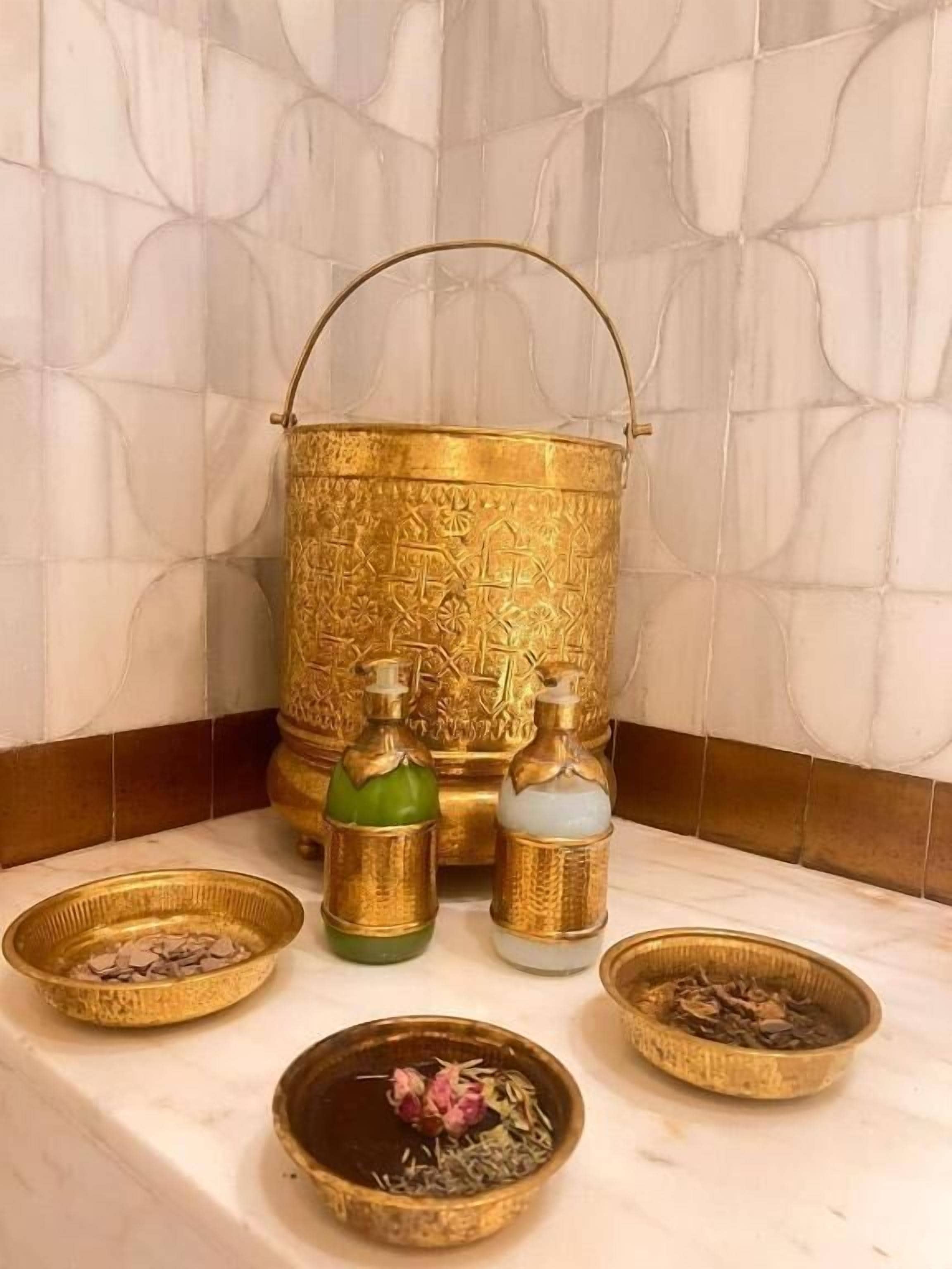 A bathroom with a marble wall, a golden basin, and two bottles of liquid.