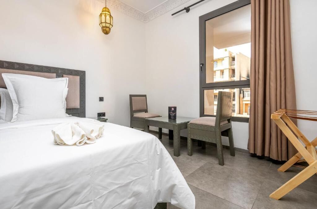 Habitación de hotel con cama, escritorio, silla, ventana con cortinas y un tendedero.