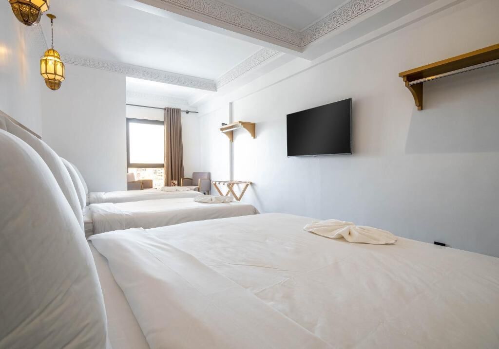 A hotel room with two beds, a flat-screen TV, and a large window with curtains.
