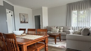 Un comedor con una mesa y sillas de madera, un sofá y una ventana con cortinas.