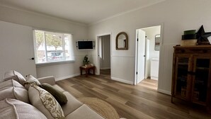 Un salón amplio con un gran ventanal, un televisor de pantalla plana, un espejo y un armario de madera.