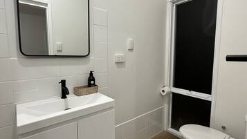 Ein modernes Badezimmer mit weißen Sanitärobjekten, Holzboden, Spiegel, Toilette und Fenster.
