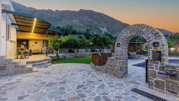 A stone patio area with outdoor seating, a stone archway, and a pool area. - Dafni Villa, A place to visit (Rethymno)