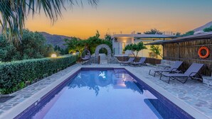 A swimming pool with lounge chairs, a stone pathway, and a view of the sunset. - Dafni Villa, A place to visit (Rethymno)