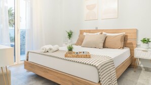 A modern bedroom with a wooden bed, a bedside table, a small plant, and a view through a glass door. - Dafni Villa, A place to visit (Rethymno)