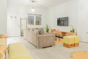 Een moderne woonkamer met een bank, voetenbankje, eethoek en een aan de muur bevestigde televisie.