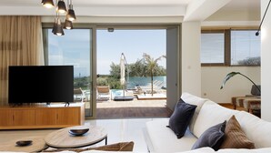 A modern living room with a flat-screen TV, a sofa, a coffee table, and a view of a pool and outdoor furniture. - Rizes Villa with Jacuzzi & Heated Pool, A Nature Paradise! (Rethymno)