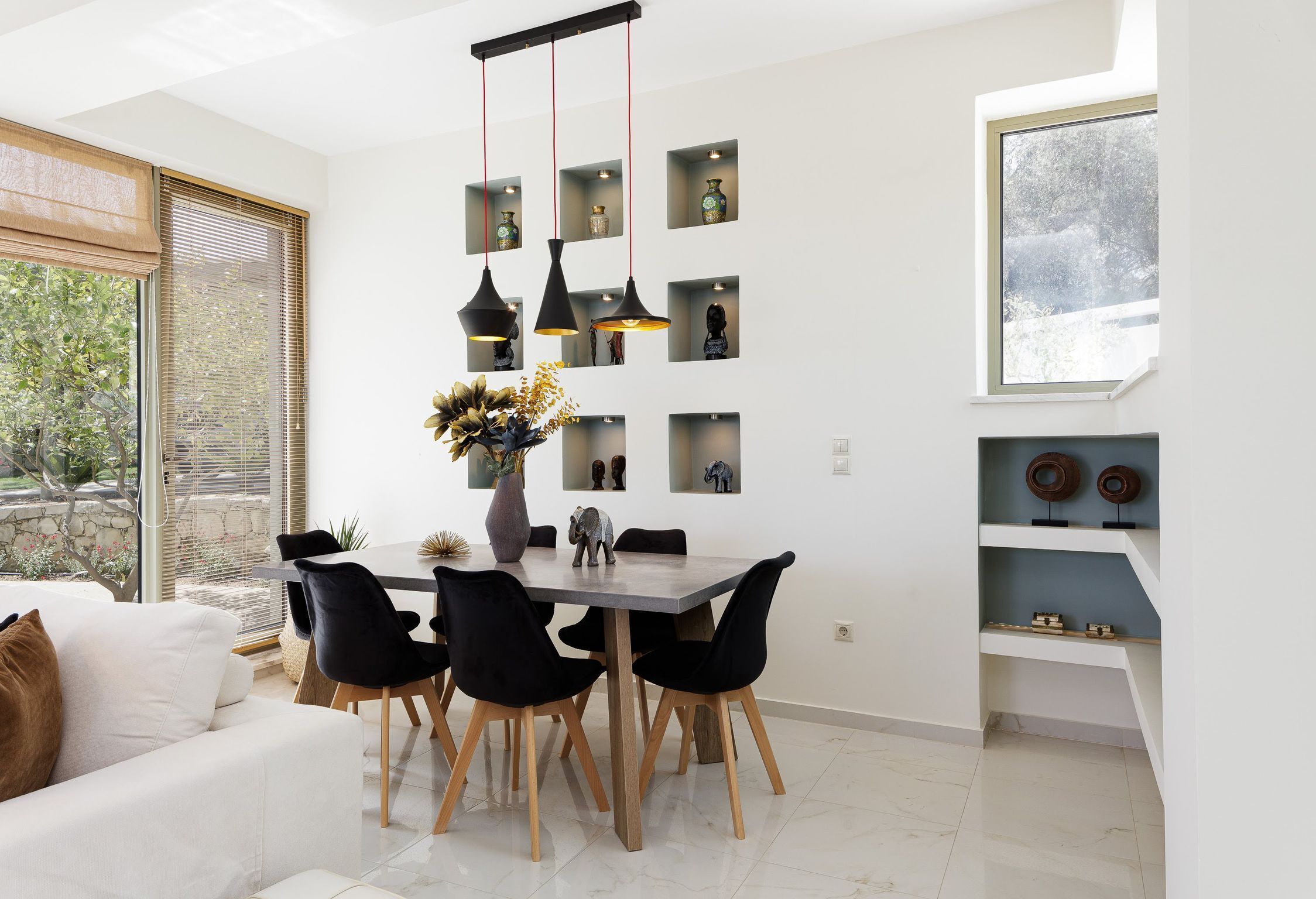 A modern dining area with a table and chairs, a vase with flowers, and shelves with decorative items.