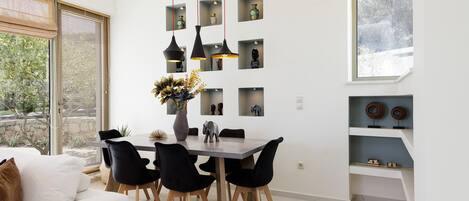 A modern dining area with a table and chairs, a vase with flowers, and shelves with decorative items.